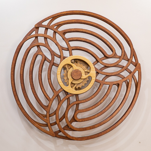Circular wooden maze sculpture featuring concentric curved channels around a pale central wheel, offering hypnotic rotating movement.