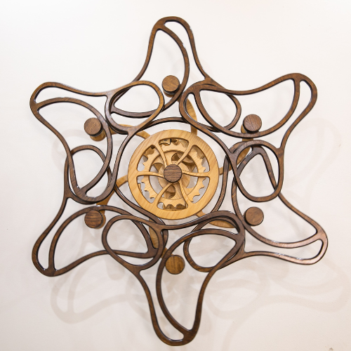 Star-shaped wall art of looping dark wooden arms encircling a light gear hub, designed for smooth, fluid kinetic motion.