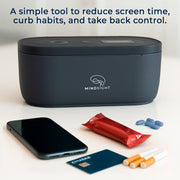 Black Mindsight timed lockbox on a table with phone, cigarettes, credit card, snack bar, and pills beside it, showing ways to curb habits