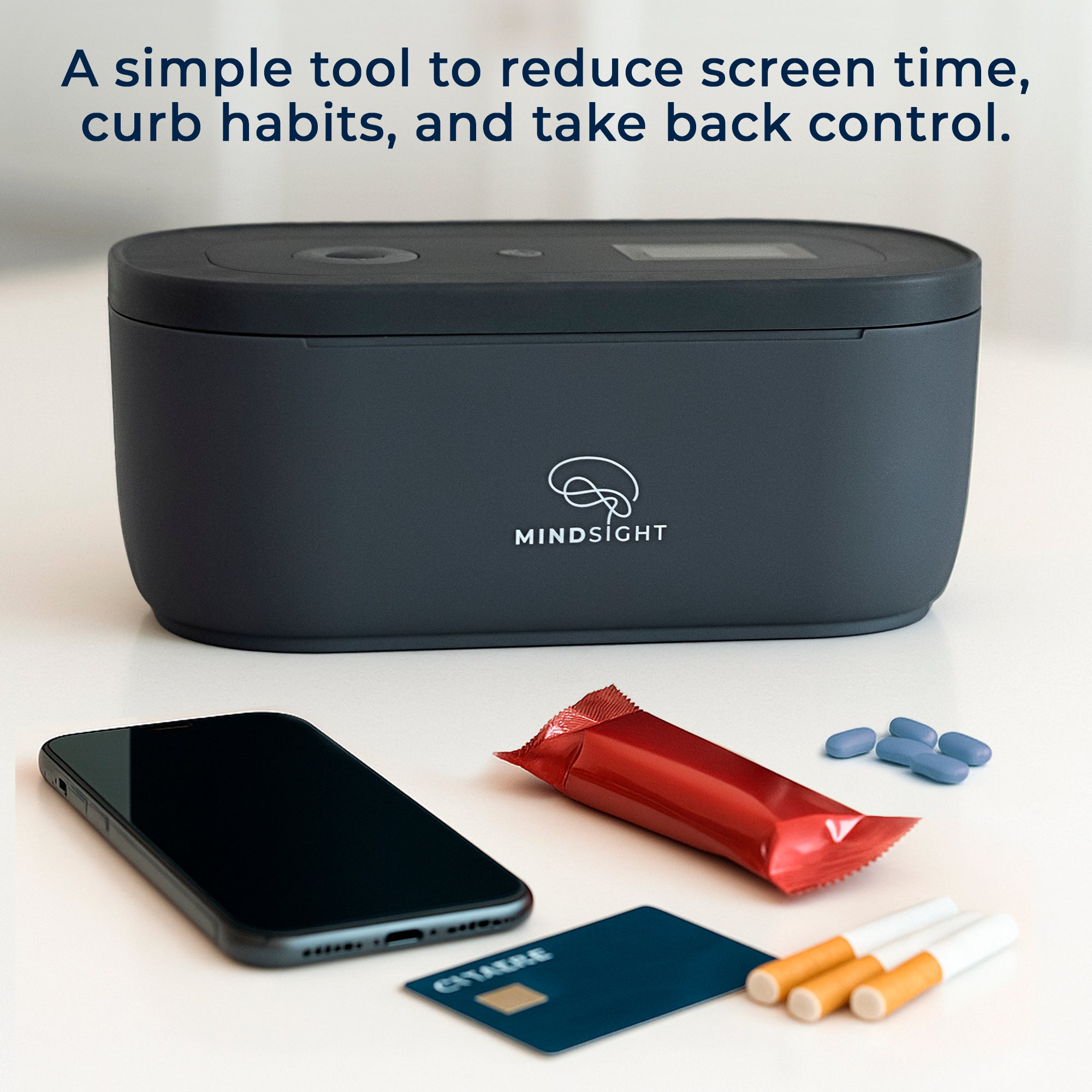 Black Mindsight timed lockbox on a table with phone, cigarettes, credit card, snack bar, and pills beside it, showing ways to curb habits