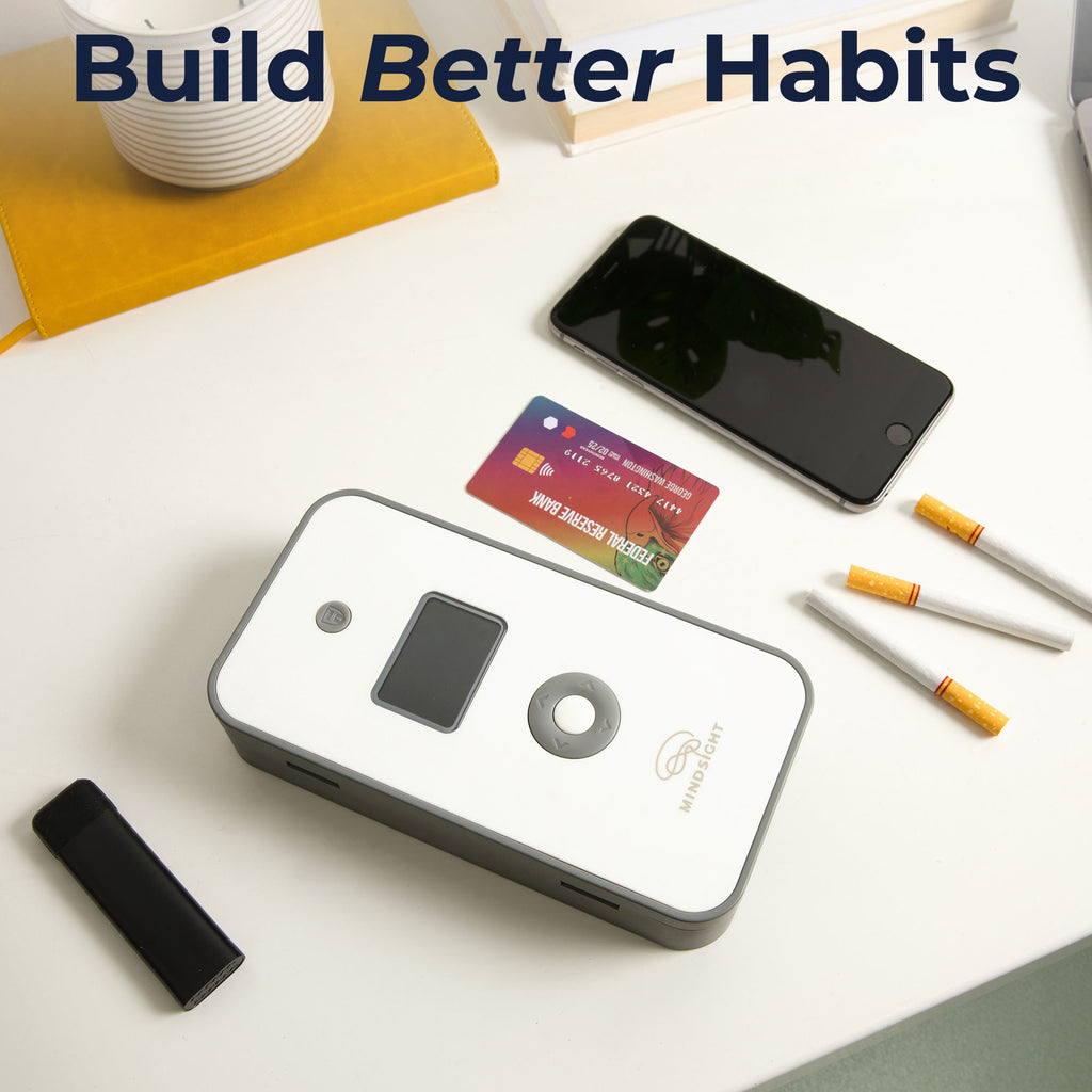 A white and gray timed lockbox placed on a desk, surrounded by items such as a phone, credit card, cigarettes, and a lighter, with text encouraging better habits.