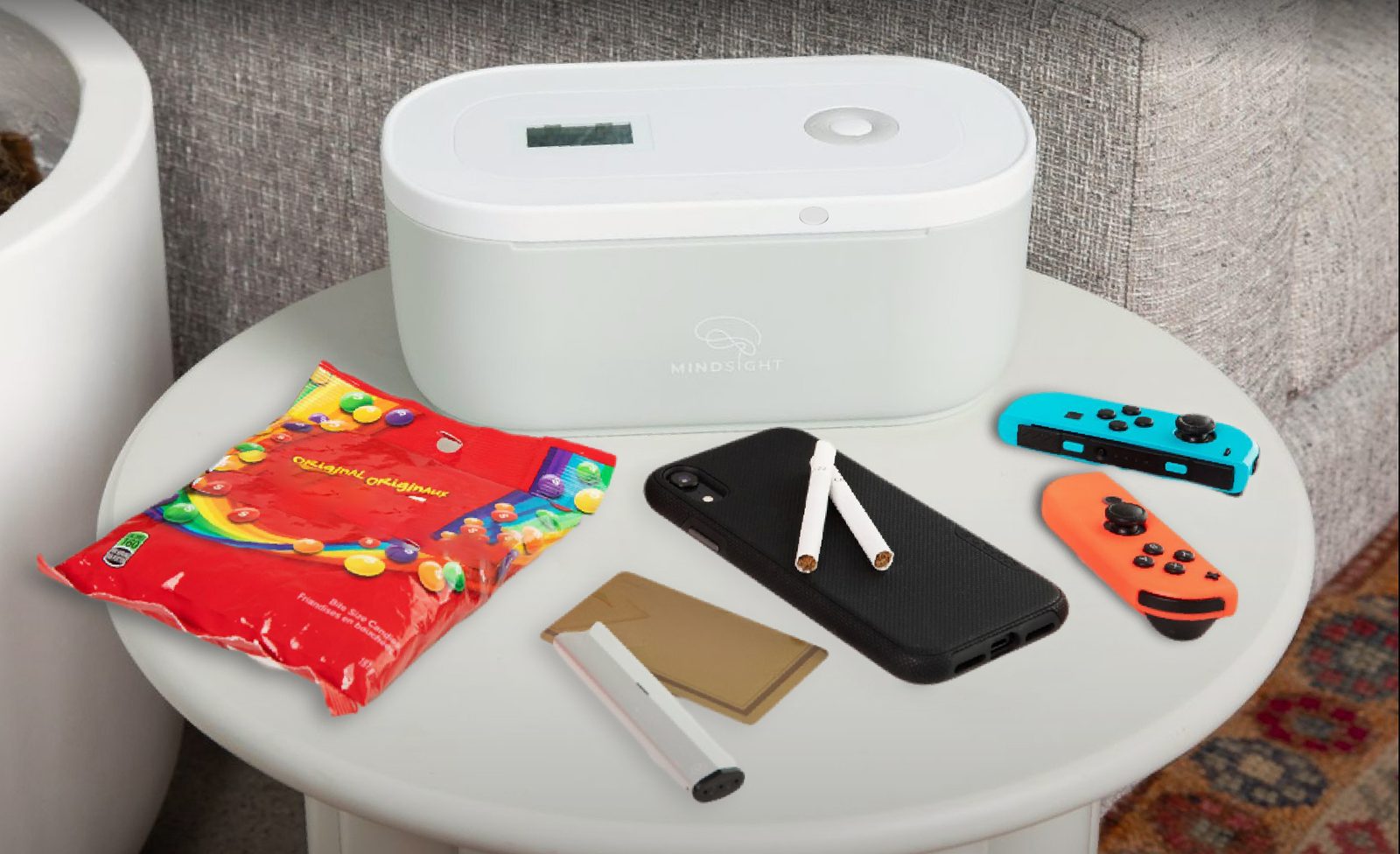 A Timed Lock Box on a side table, with a phone, snacks, a vape, and cards beside it